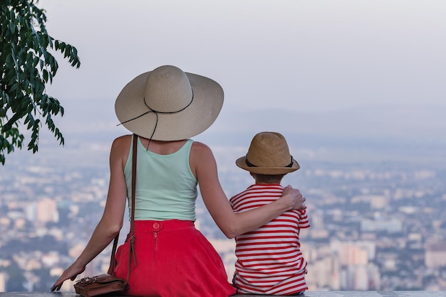 Belle jeune femme au grand chapeau de paille étreint le petit garçon et regarde le panorama de la ville Vue arrière