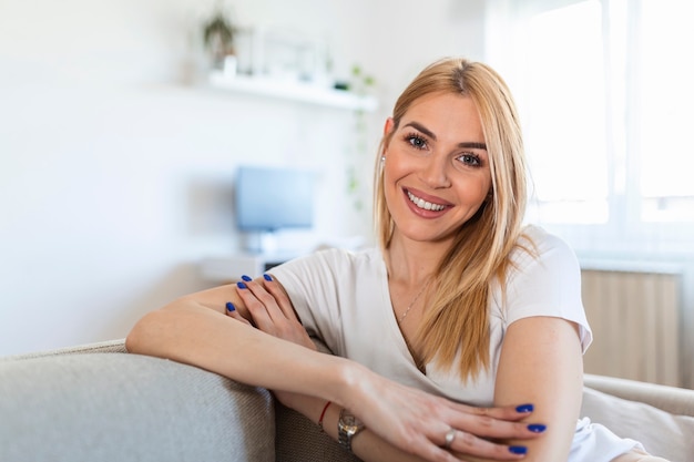 Belle jeune femme aux cheveux blonds assis sur le canapé. Portrait d'une jeune femme souriante à la maison dans une belle pièce lumineuse