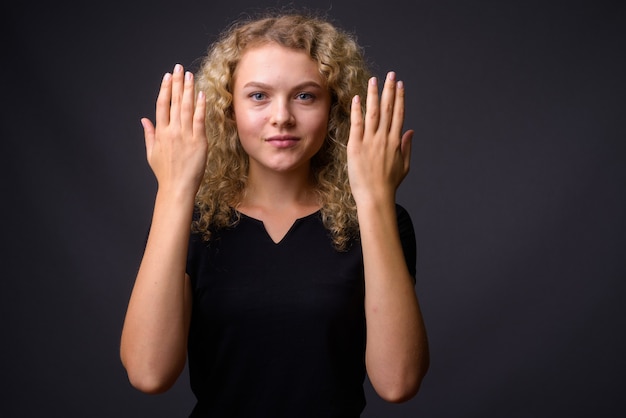 Belle jeune femme aux cheveux blonds bouclés contre backgro gris