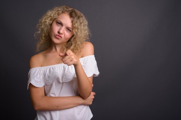 Belle jeune femme aux cheveux blonds bouclés contre gris