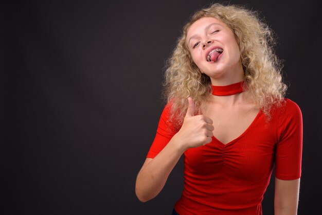 Belle jeune femme aux cheveux blonds bouclés contre gris