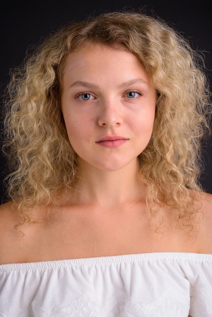 Belle jeune femme aux cheveux blonds bouclés contre gris