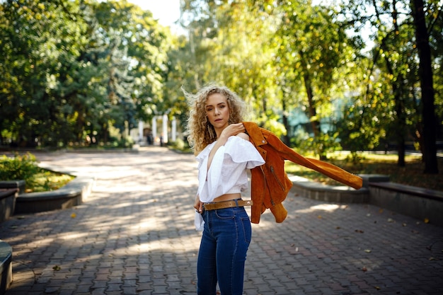 Une belle jeune femme aux cheveux blonds bouclés se promène dans la ville ensoleillée, bénéficie d'un déjeuner à pied