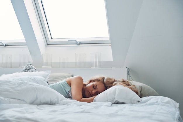 Belle jeune femme aux cheveux blonds dormant dans son lit et recouverte d'une couverture