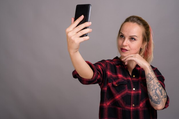 Belle jeune femme aux cheveux blonds portant une chemise à carreaux rouge sur fond gris