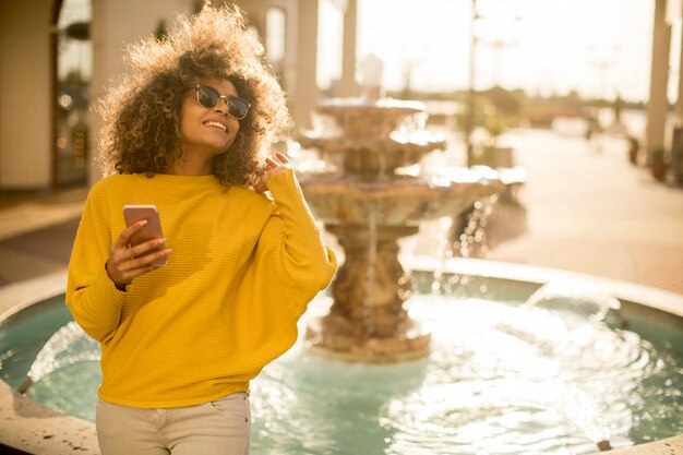 Belle jeune femme aux cheveux bouclés à l'aide de son téléphone portable à écran tactile