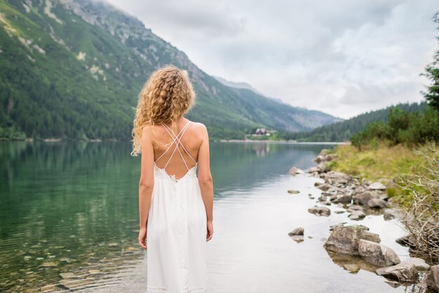 Belle jeune femme aux cheveux bouclés dans une robe blanche se tient près de