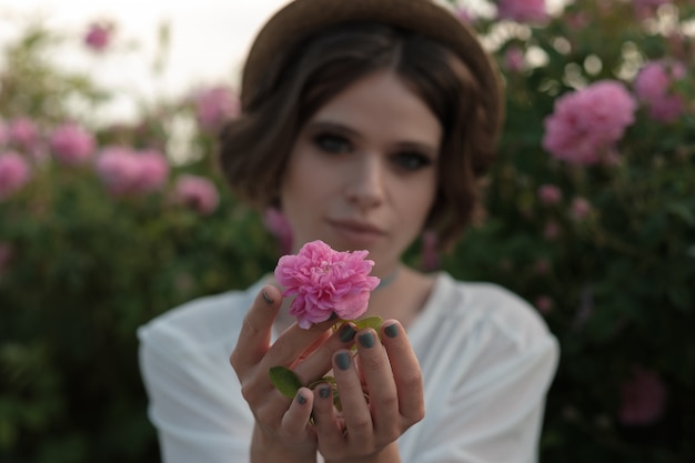 Belle jeune femme aux cheveux bouclés posant près de roses dans un jardin. Le concept de la publicité des parfums.