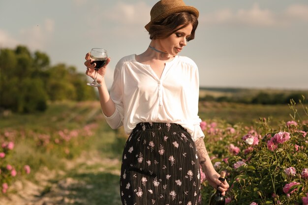 Belle jeune femme aux cheveux bouclés posant près de roses dans un jardin. Le concept de la publicité des parfums.