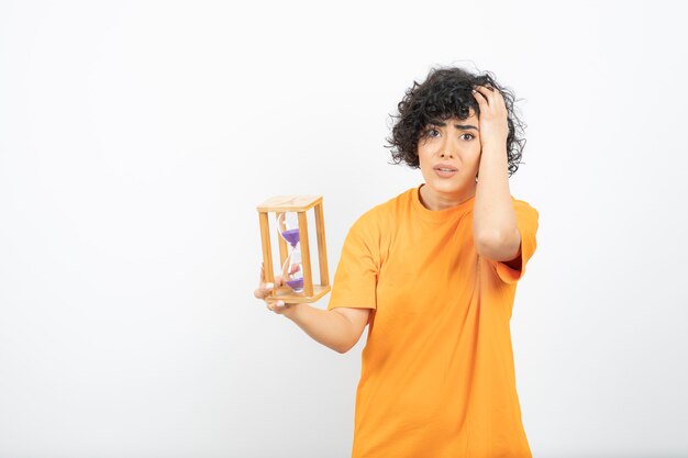 Belle jeune femme aux cheveux bouclés tenant le sablier.