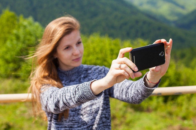 Belle jeune femme aux cheveux bruns fait selfie sur son téléphone sur le fond de la nature verte