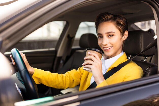 Belle jeune femme aux cheveux courts conduit une voiture dans la ville