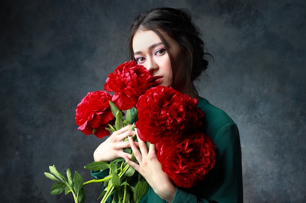 Belle jeune femme aux cheveux longs dans une robe verte avec un gros bouquet de pivoines