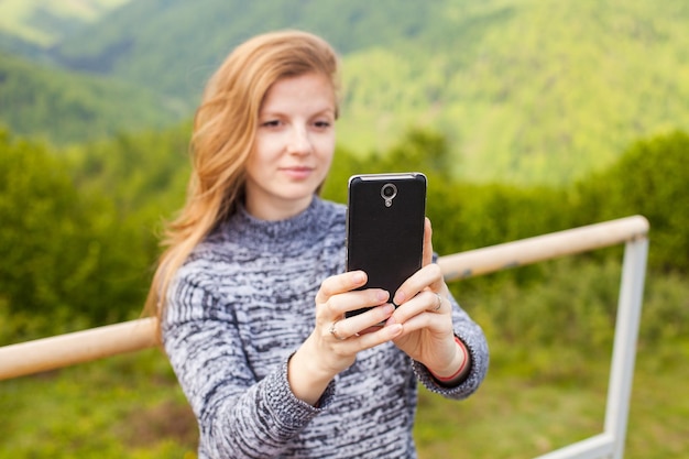 Photo belle jeune femme aux cheveux longs fait selfie sur son téléphone noir avec un sourire sur le fond de la nature