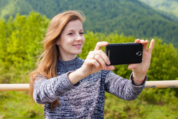 Belle jeune femme aux cheveux longs fait selfie sur son téléphone avec un sourire sur le fond de la nature verte