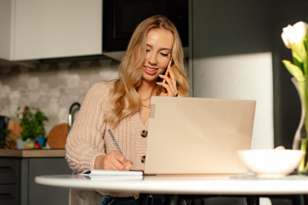 Belle jeune femme aux cheveux longs travaille en ligne à la maison sur son ordinateur portable et prend des commandes sur lui