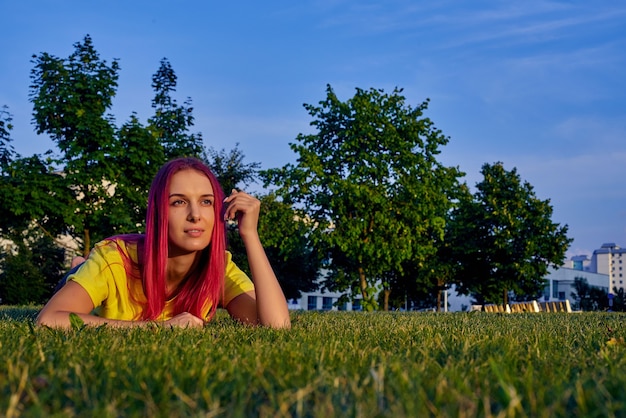 Belle jeune femme aux cheveux roses se trouve sur le ventre sur la pelouse dans un parc de la ville