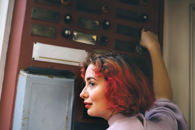 Belle jeune femme aux cheveux rouges sonne à la porte d'un immeuble