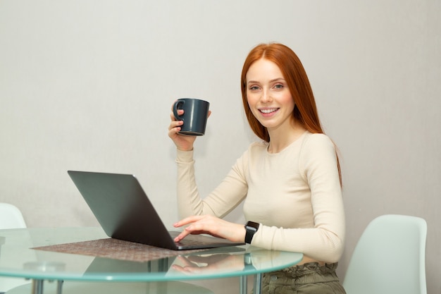 belle jeune femme aux cheveux rouges à la table avec un ordinateur portable
