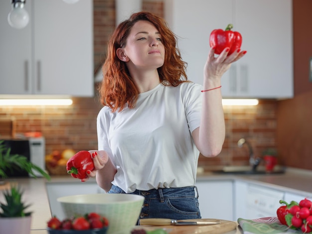 Belle jeune femme aux cheveux roux prépare une salade de légumes dans la cuisine