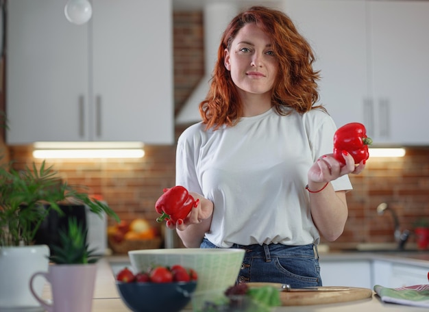 Belle jeune femme aux cheveux roux prépare une salade de légumes dans la cuisine