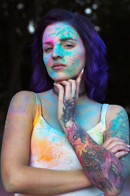 Belle jeune femme aux cheveux violets et tatouage sur son bras recouvert de poudre Holi colorée