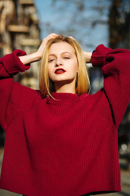 Belle jeune femme aux lèvres rouges portant un pull en tricot posant dans les rayons du soleil
