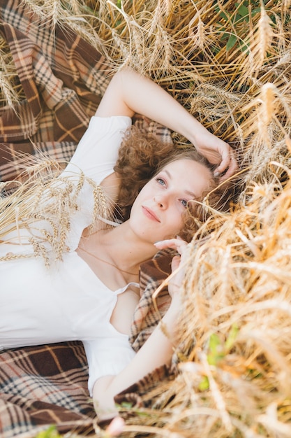 Belle jeune femme aux longs cheveux bouclés pose dans un champ de blé en été au coucher du soleil