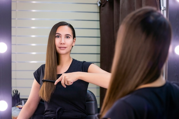 Belle jeune femme aux longs cheveux bruns lisses s'occupe de ses cheveux