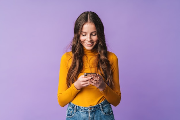 Belle jeune femme aux longs cheveux bruns souriant et tenant un téléphone portable isolé