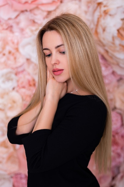 Belle jeune femme aux longs cheveux raides sur fond de mur de fleurs