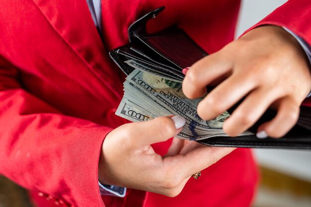 Belle jeune femme aux mains fragiles sort beaucoup de dollars de son sac à main