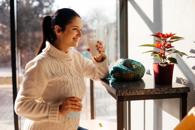 Belle jeune femme ayant du temps pour elle-même au café après avoir fini ses achats Belle fille souriante buvant du café au café assis seul près de la fenêtre