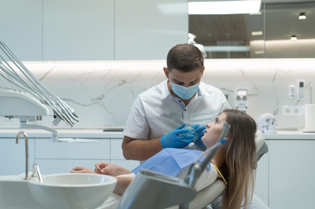 Belle jeune femme ayant un traitement dentaire chez le dentiste. Docteur montrant la mâchoire. Concept de dents saines.