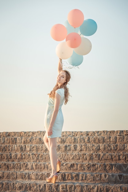 Belle jeune femme avec des ballons multicolores volants contre le ciel. concept de bonheur et de rêves