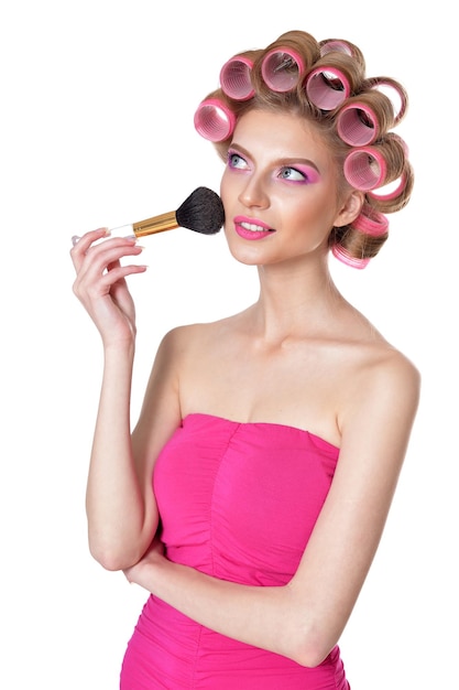 Belle jeune femme avec des bigoudis roses tenant un pinceau de maquillage