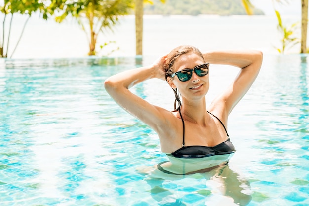 Belle jeune femme en bikini noir relaxant dans la piscine de l'hôtel