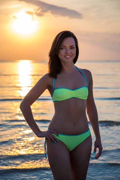 Belle jeune femme en bikini sur la plage au coucher du soleil