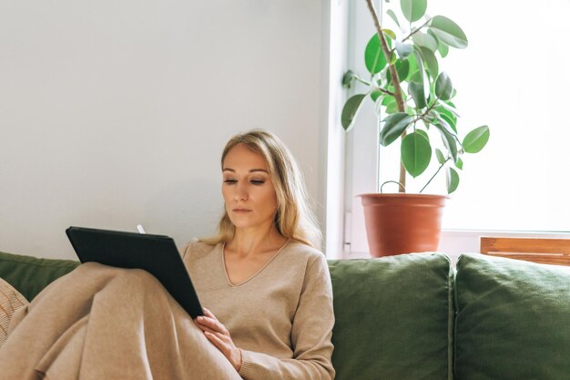 Belle jeune femme blonde artiste illustratrice dessinant sur une tablette près de la fenêtre à la maison