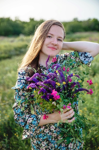 Photo belle jeune femme blonde aux cheveux longs d'apparence européenne avec un bouquet fleuri de fleurs sauvages...