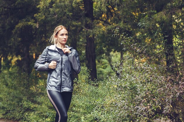 Belle jeune femme blonde aux cheveux longs est en cours d'exécution dans le parc à jour de pluie,