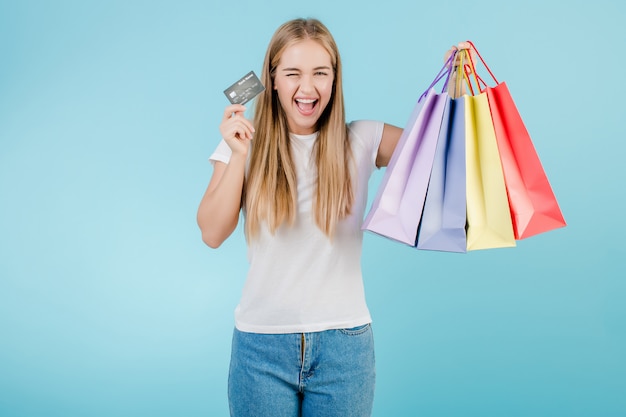 Belle jeune femme blonde avec carte de crédit et des sacs colorés, isolés sur bleu