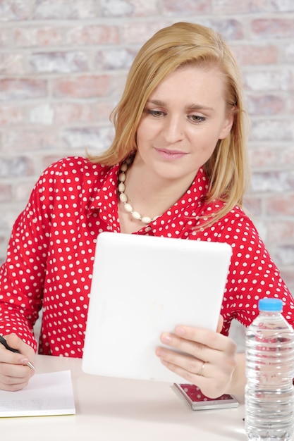 Belle jeune femme blonde avec une chemise rouge et une tablette