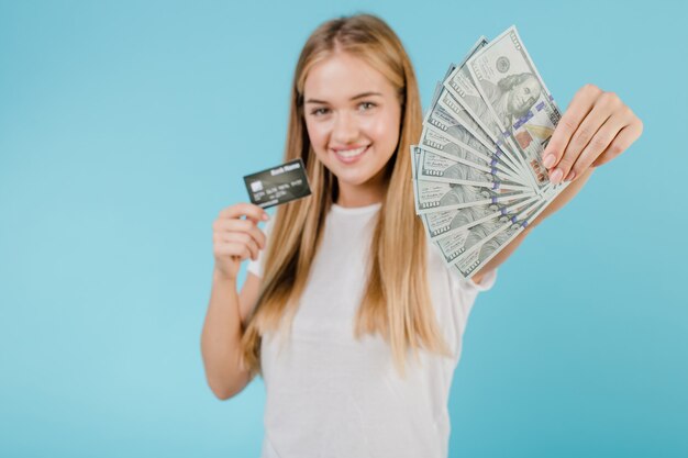 Belle jeune femme blonde avec dollar en argent et carte de crédit isolée sur bleu