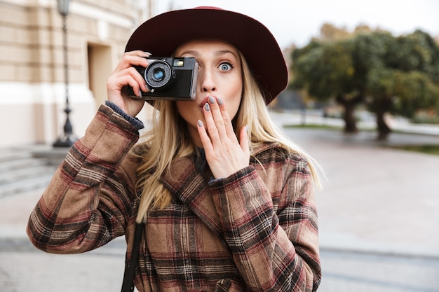 Belle jeune femme blonde élégante portant un manteau marchant à l'extérieur, prendre des photos avec un appareil photo