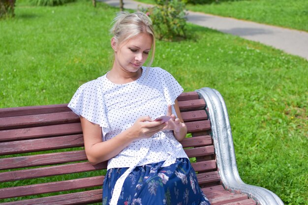 belle jeune femme blonde est assise sur un banc extérieur avec téléphone