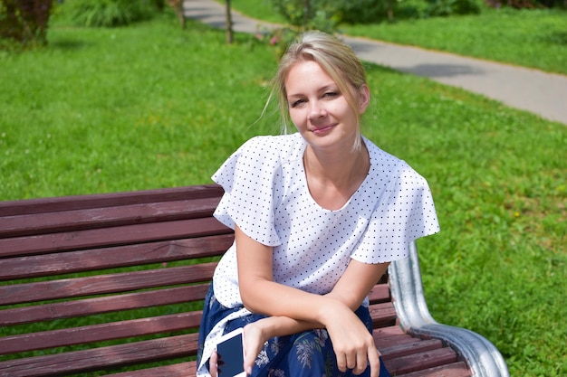 belle jeune femme blonde est assise sur un banc extérieur avec téléphone