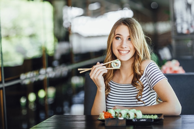 Une belle jeune femme blonde mangeant des sushis sur la terrasse d'été d'un restaurant japonais