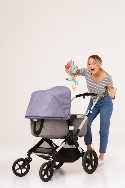 belle jeune femme blonde optimiste positive mère marchant avec bébé dans un landau isolé sur un mur blanc.