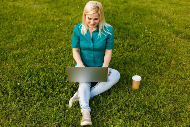 belle jeune femme blonde avec un ordinateur portable dans le parc par une chaude journée d'été